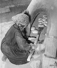 Woman removing small loaves from clay oven