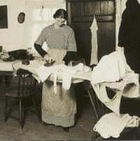 Woman in long skirt using flat iron ironing on board supported by chairs