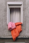 Bright orange duvet and two pillows hanging out of window in concrete apartment building